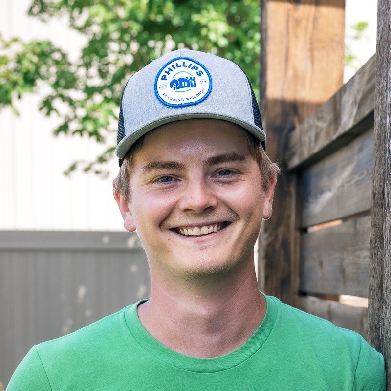 Smiling man wearing cap outdoors by wooden fence