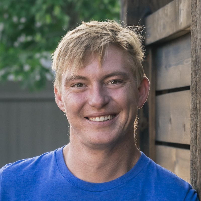 Smiling person with short blond hair outdoors