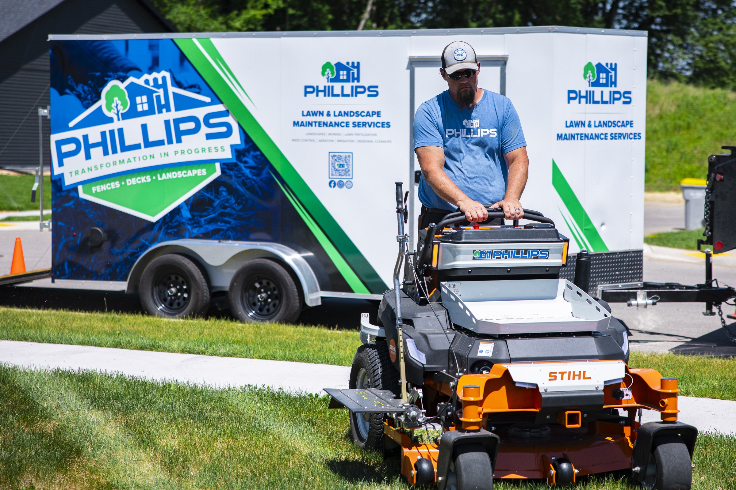 Landscaper mowing lawn beside branded service trailer