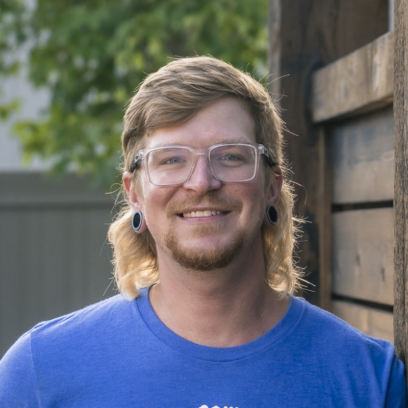 Smiling man with glasses and mullet hairstyle outdoors