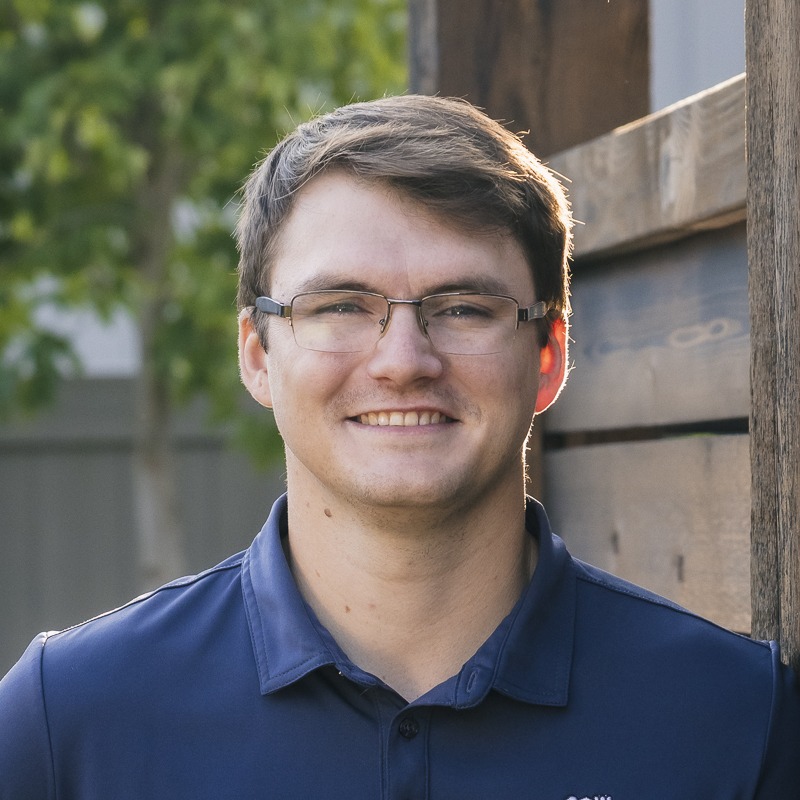 Smiling man with glasses outdoors by wooden wall