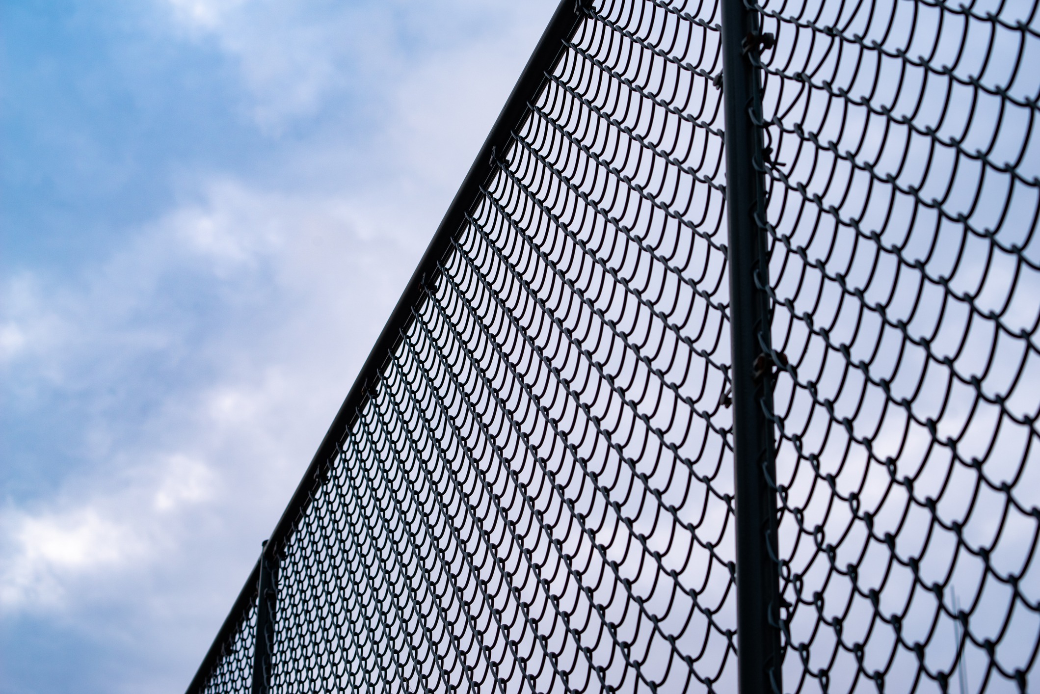 Chain-link fence against cloudy blue sky