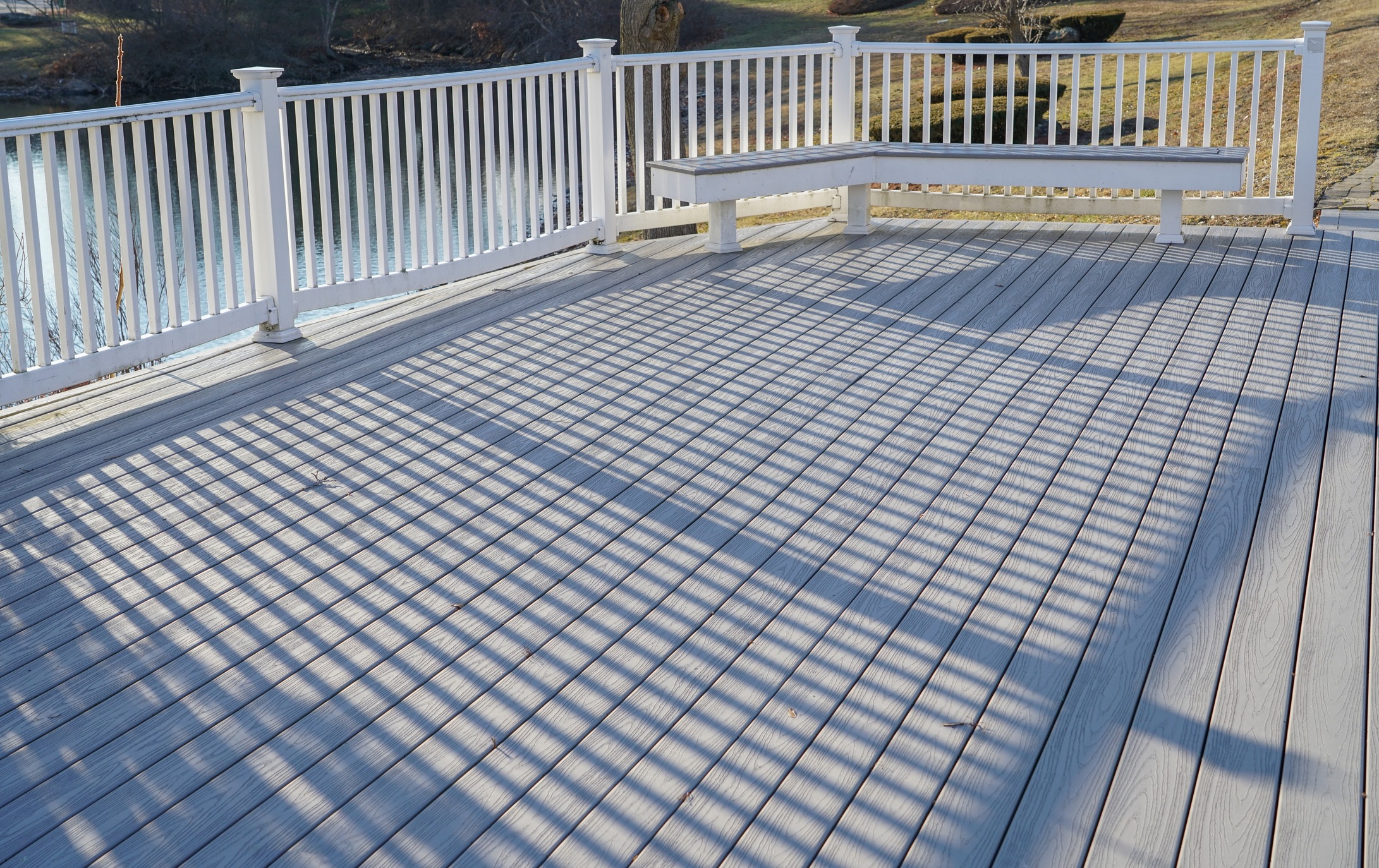 Sunlit wooden deck with white railing and bench