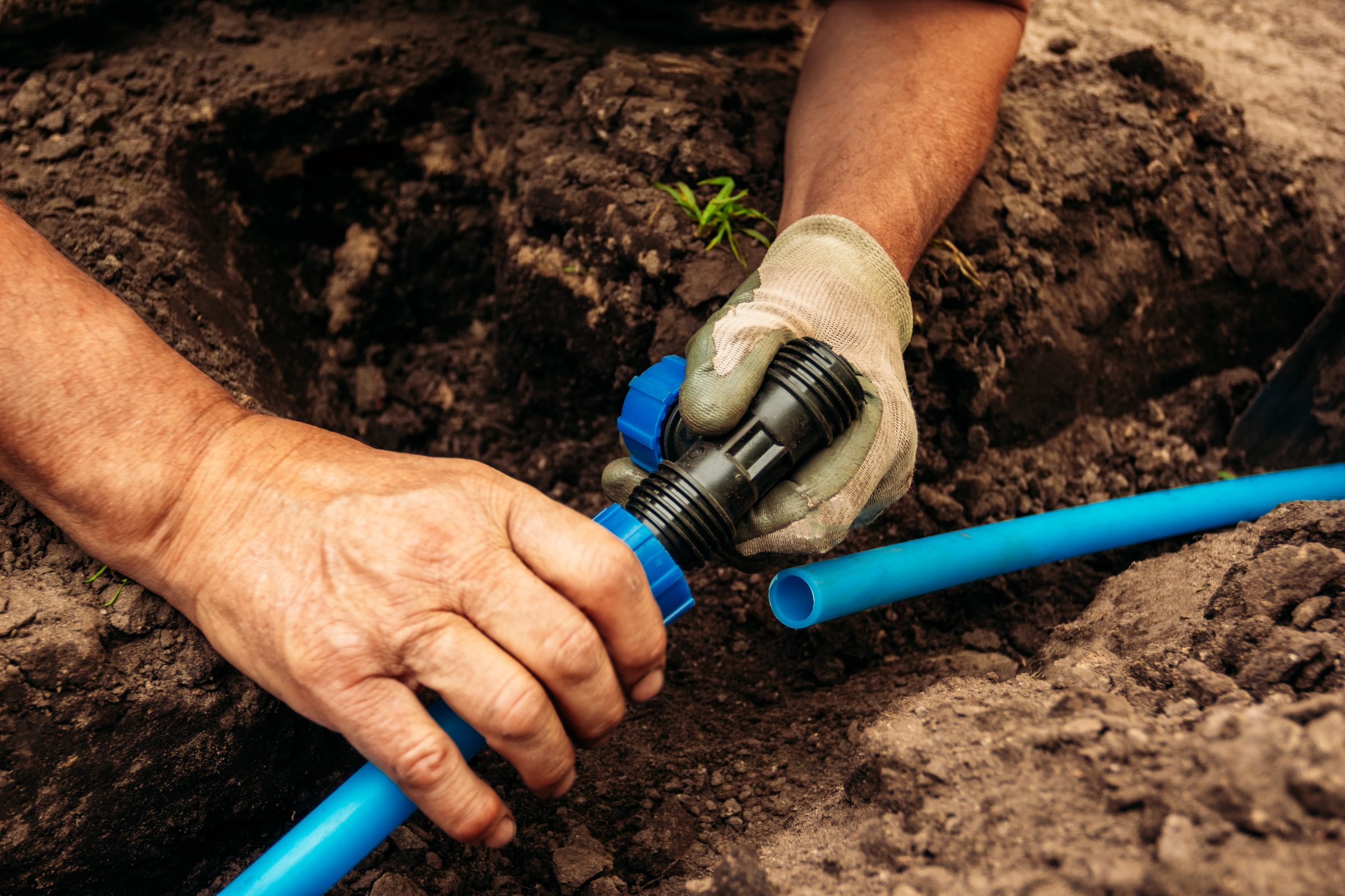 Hands connecting blue irrigation pipe in soil trench