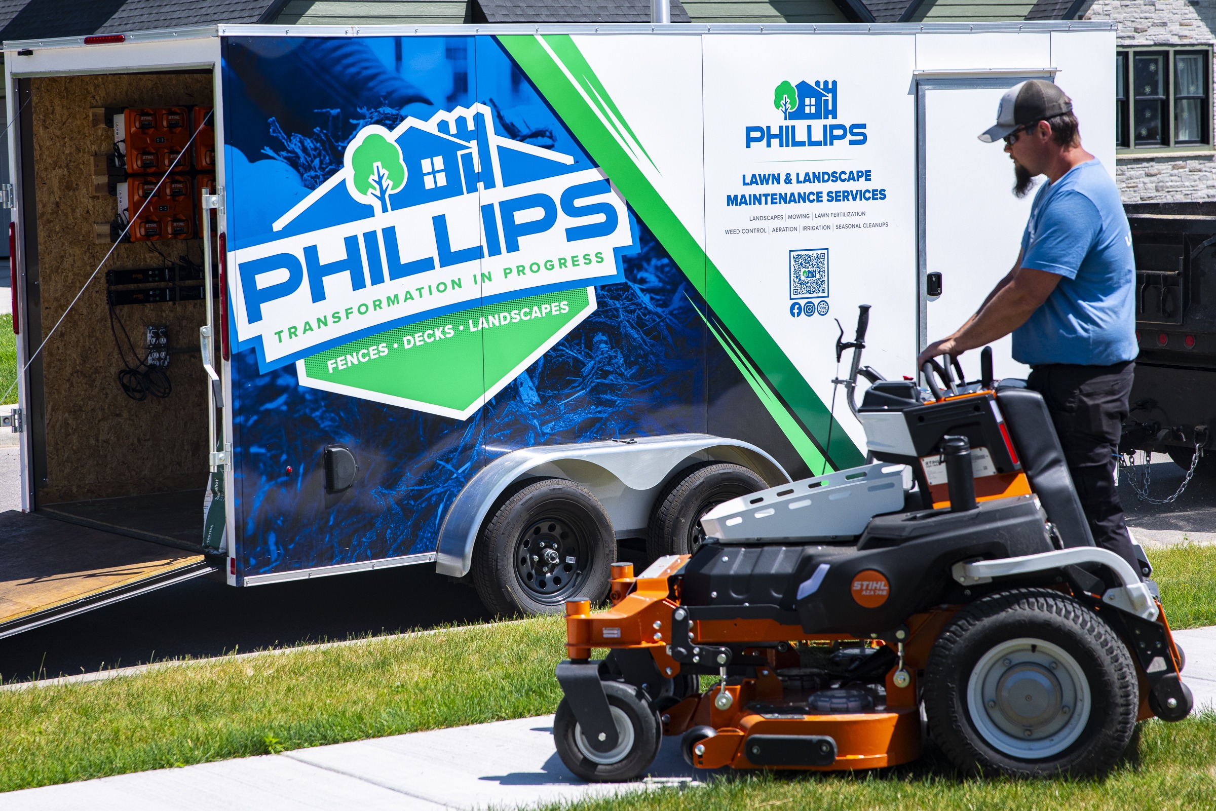 Landscaper mowing lawn beside branded service trailer