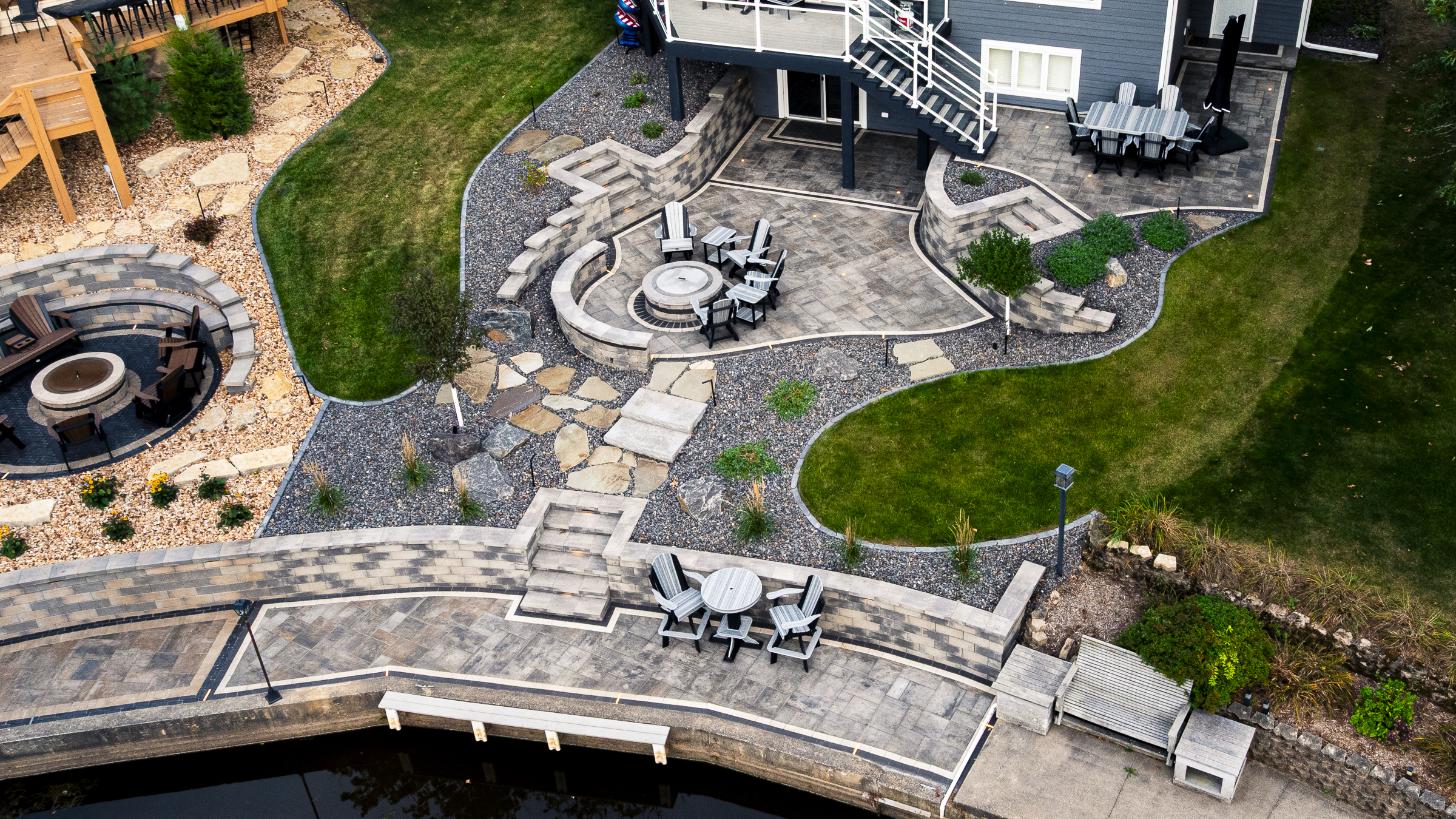 Aerial view of tiered backyard patio with retaining walls, steps, patio areas, lighting,softscaping and a fire pit in Mauston, WI on Castle Rock Lake.