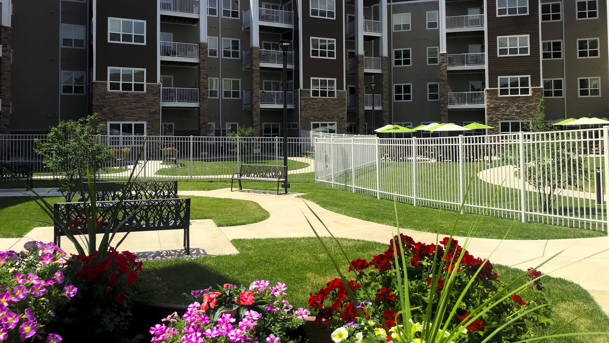 Eagle Crest Apartment courtyard with benches, lawn, flowers, and a white aluminum fence.
