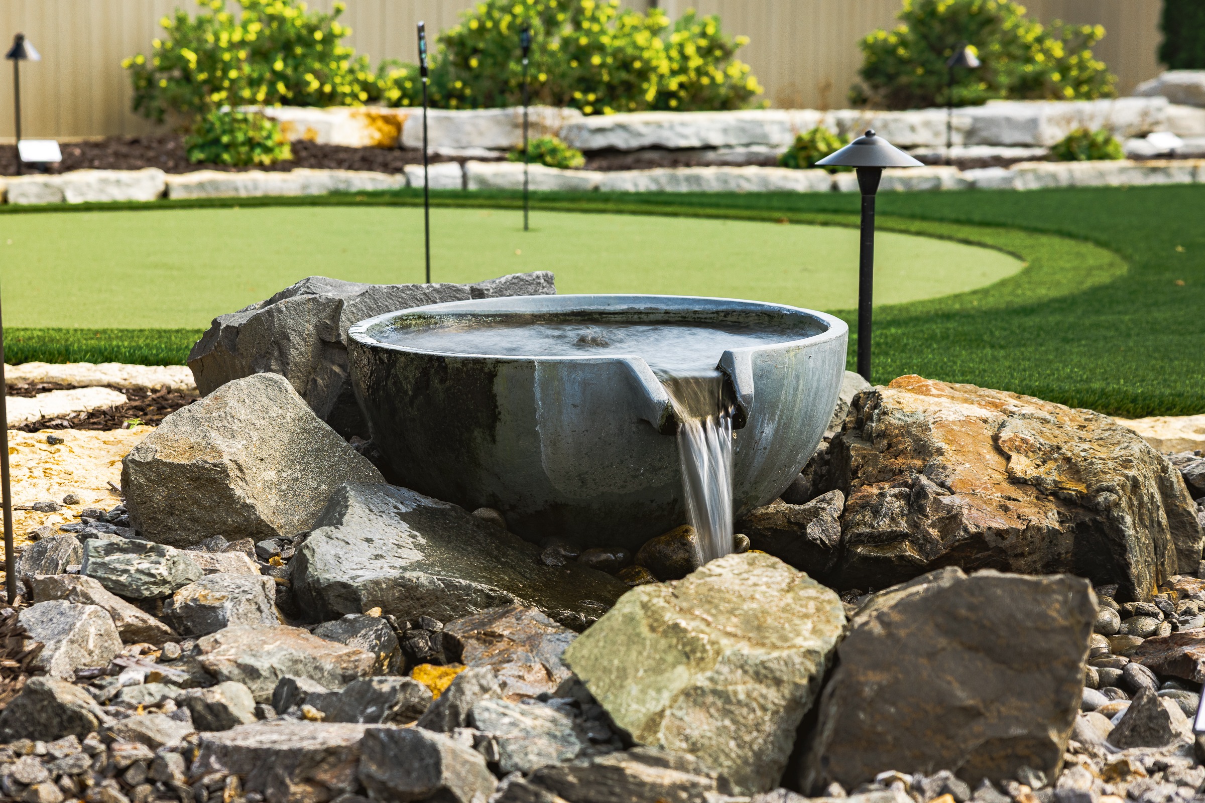 Modern stone fountain beside backyard putting green