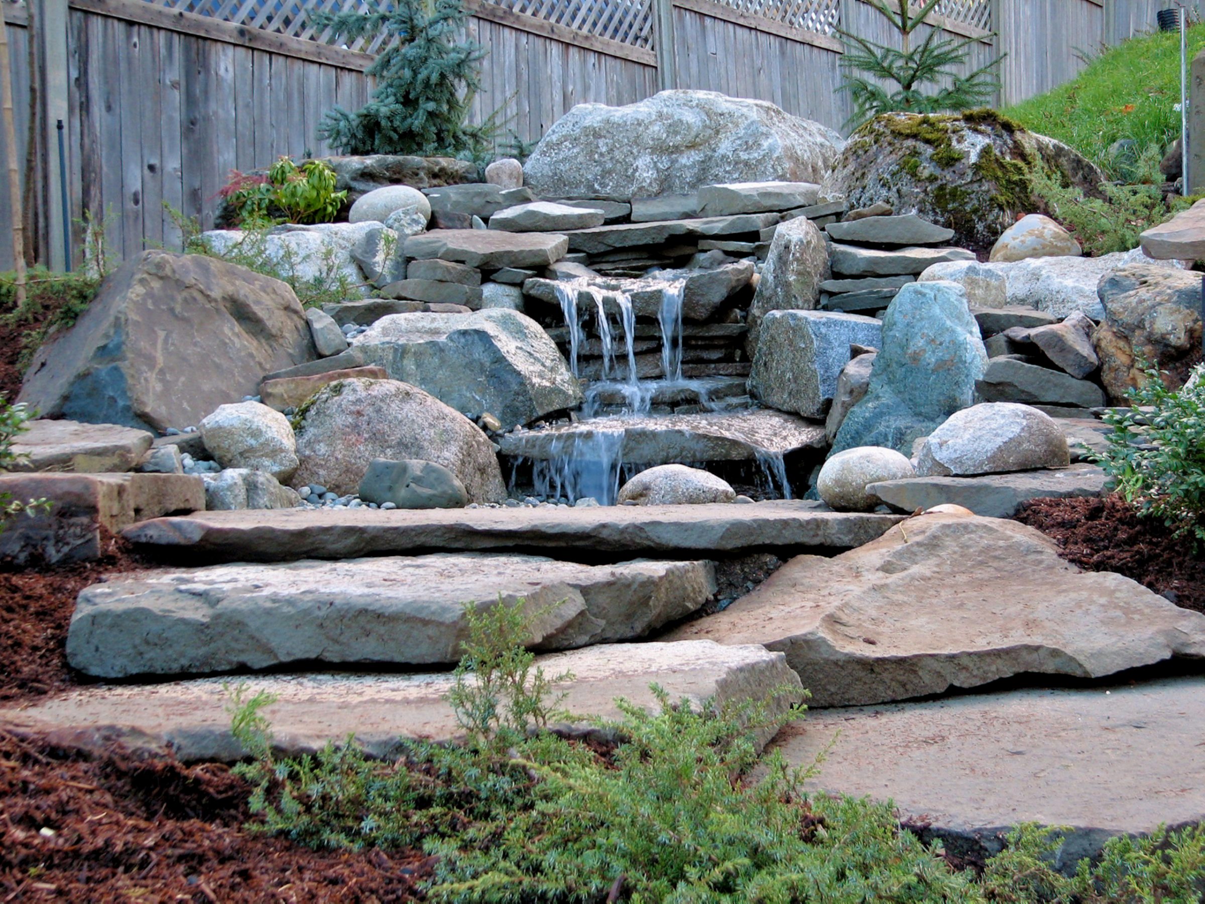 Backyard stone waterfall with landscaped garden rocks