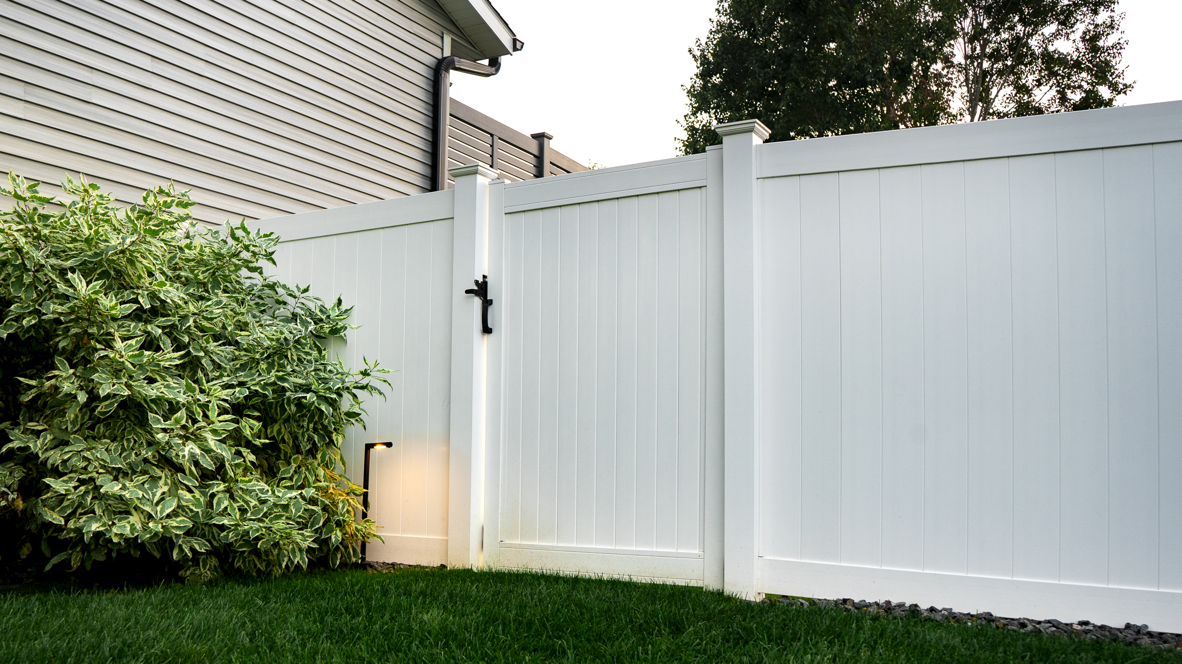 White vinyl privacy fence with gate and low-voltage lighting.